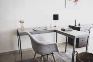 picture of a home office with L shaped desk with closed laptop on the left return and a basic home chair